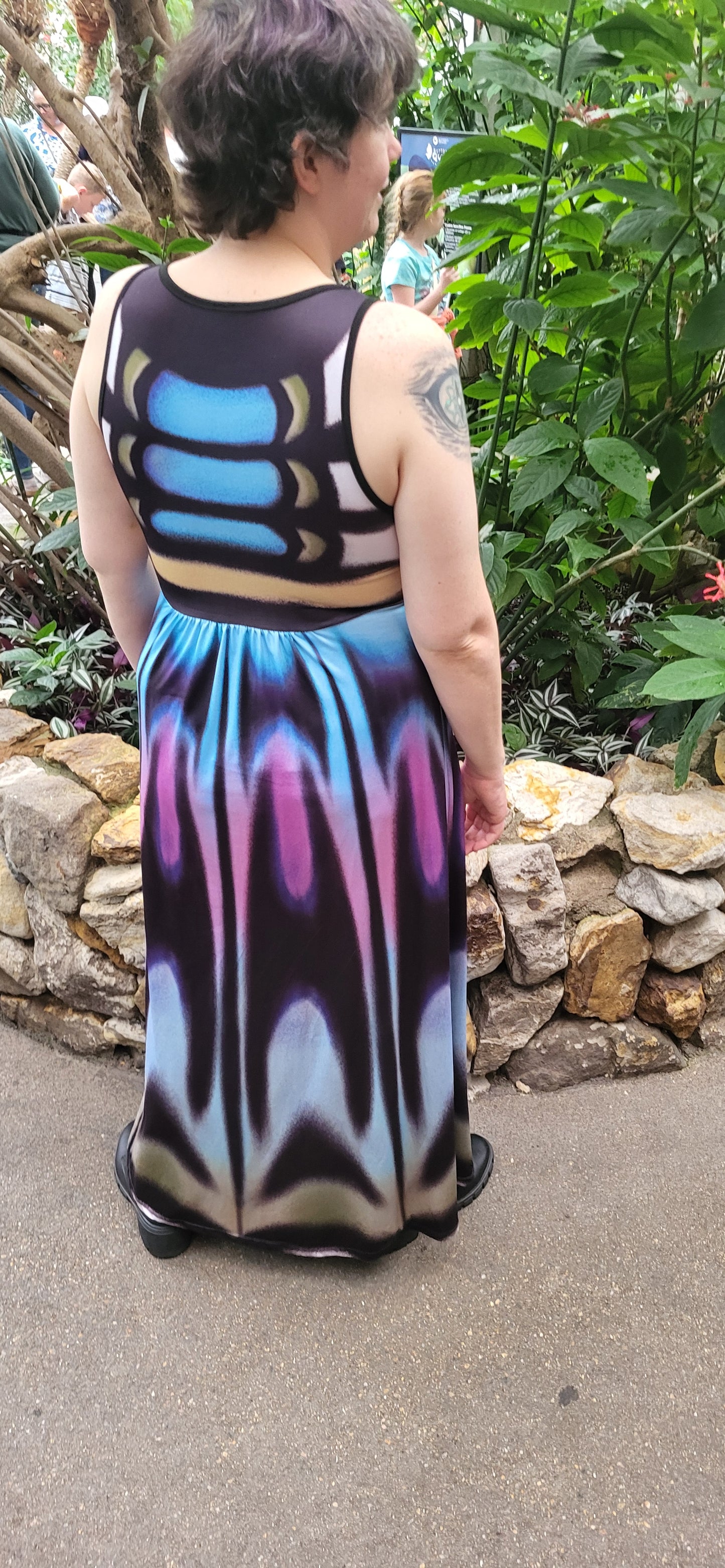 Person wearing a colorful dress with abstract patterns standing outdoors on a stone path. Inspired by the clipper butterfly.
