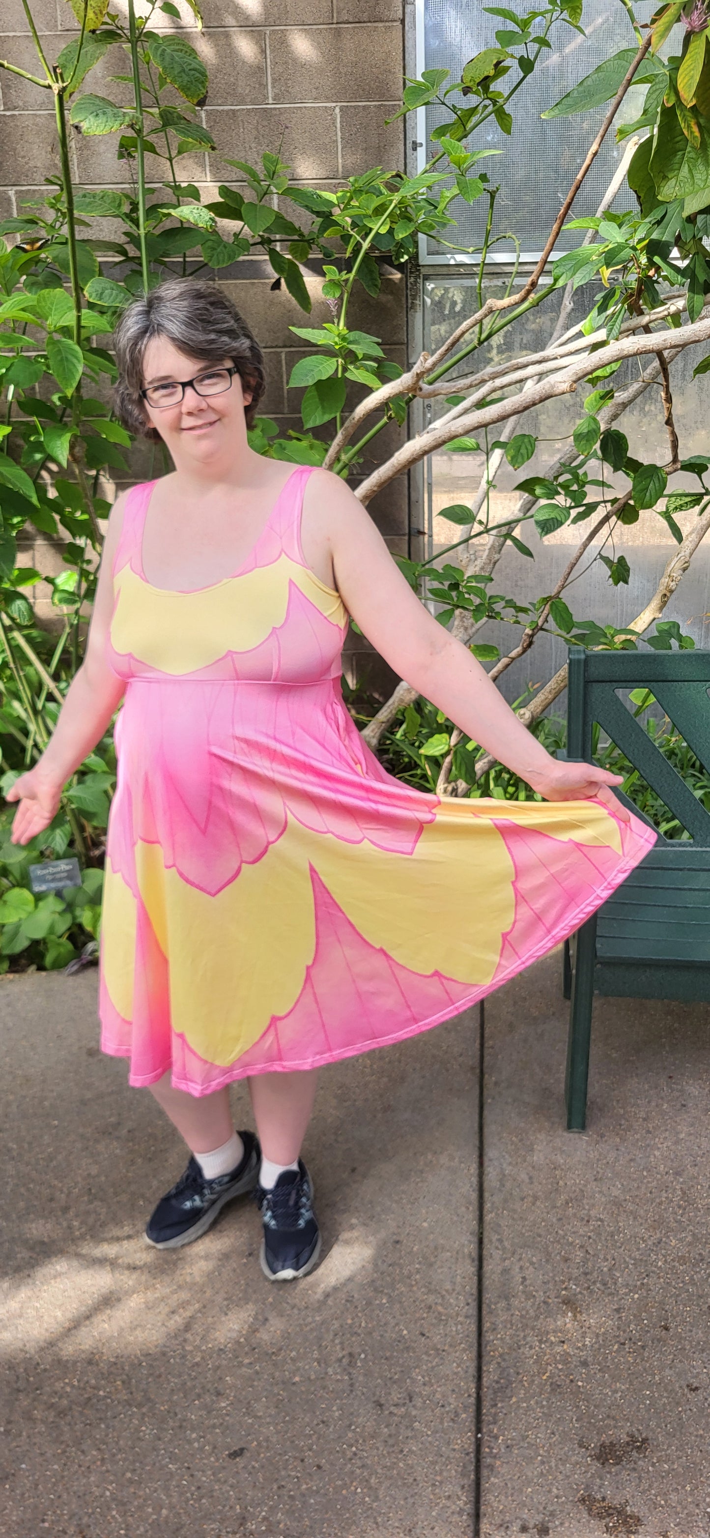 Person wearing a pink and yellow dress standing outdoors next to a plant.