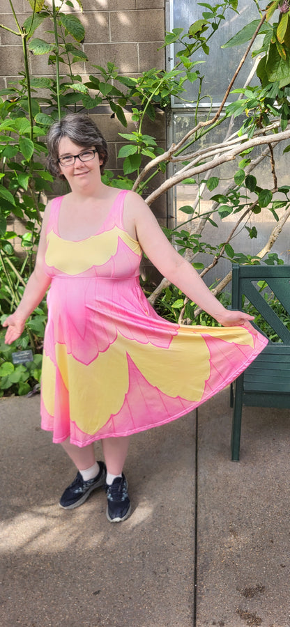 Person wearing a pink and yellow dress standing outdoors next to a plant.