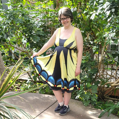Person wearing a tiger swallowtail dress standing on a concrete path with greenery in the background