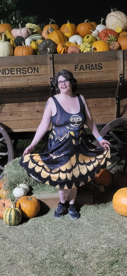 A woman wearing a deathhead moth dress  stands in front of a wooden wagon filled with pumpkins at night. The wagon is labeled 'ANDERSON FARMS'.